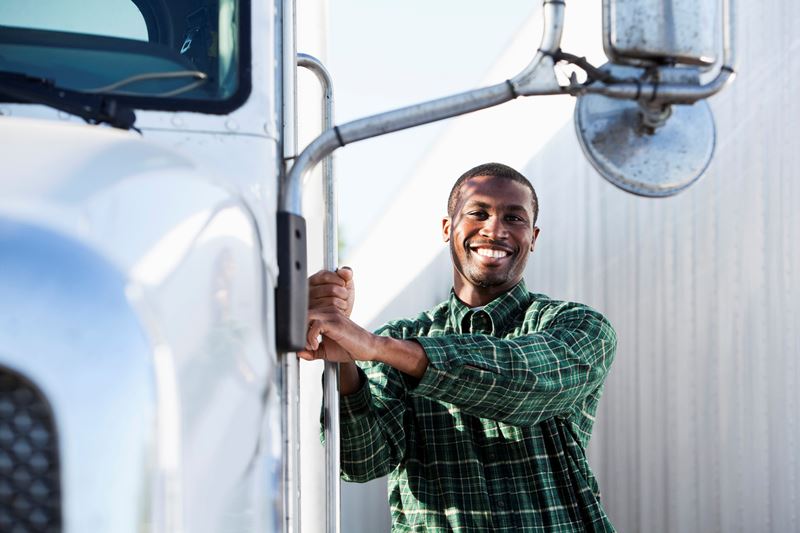 Un homme souriant à la caméra s'accroche à la porte de son camion